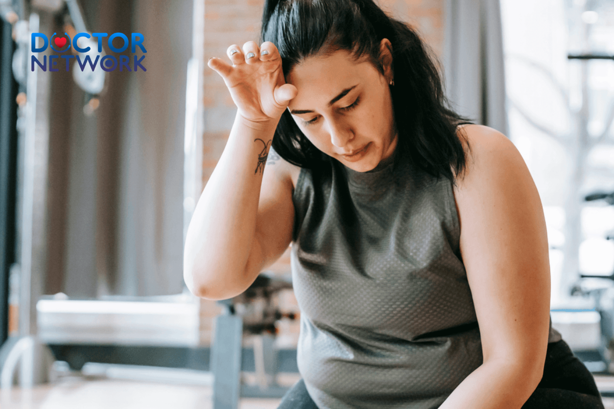 A woman looking exhausted and wiping sweat after an intense workout session at the gym, showing signs of physical fatigue.